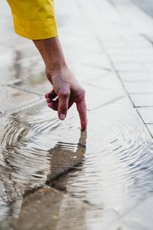 Die Hand einer Frau berührt eine Regenpfütze auf der Straße - EBBF01245