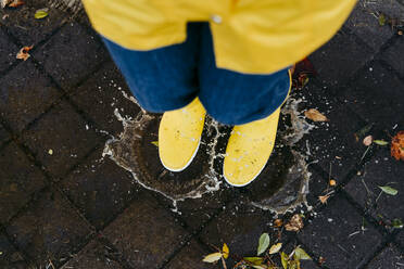 Frau mit gelben Stiefeln springt in der Regenzeit in eine Pfütze - EBBF01248