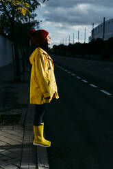 Frau mit gelbem Regenmantel und geschlossenen Augen steht bei Sonnenuntergang auf der Straße - EBBF01259