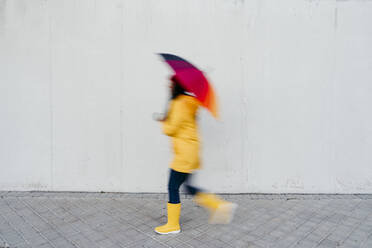 Frau mit buntem Regenschirm auf dem Fußweg an der Mauer - EBBF01273