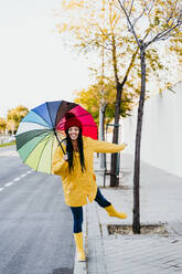 Frau mit hochgelegtem Bein, die einen bunten Regenschirm auf einem Fußweg hält - EBBF01275