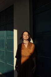 Woman with eyes closed standing by door in resort at Deauville, France - OGF00658