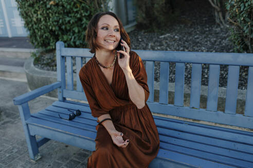 Lächelnde Frau, die in einem Ferienort in Deauville, Frankreich, mit ihrem Mobiltelefon spricht - OGF00666