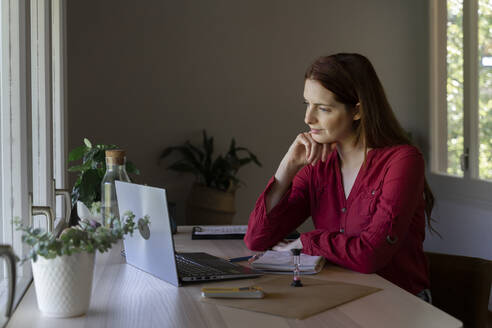 Psychologist with head in hands listening to video call on laptop while sitting at home - AFVF07448