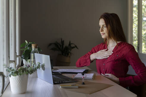 Doctor showing breathing therapy on video call through laptop while sitting at home - AFVF07451