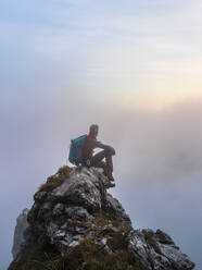 Nachdenklicher Wanderer bei Sonnenaufgang auf einem Berggipfel in den Bergamasker Alpen, Italien - MCVF00644