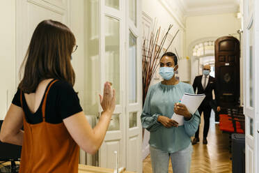 Female stopping businesswoman with protective face mask in corridor - JRFF04802