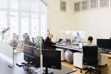 Geschäftsleute mit Schutzmaske bei der Arbeit am Schreibtisch im Büro - JRFF04806