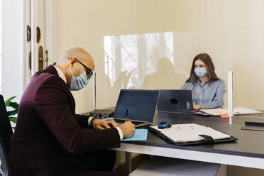 Männliche und weibliche Unternehmer mit Schutzmaske bei der Arbeit im Büro - JRFF04810