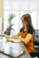 Lächelnde Geschäftsfrau, die am Schreibtisch Tagebuch liest - JRFF04835