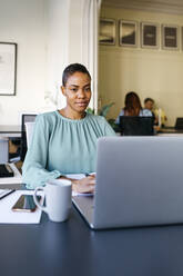 Smiling businesswoman working on laptop at office desk - JRFF04838