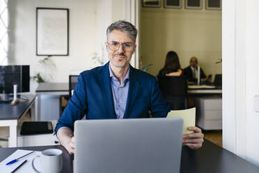 Smiling confident businessman working on laptop at office desk - JRFF04843