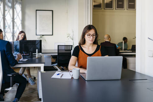 Selbstbewusste Geschäftsfrau bei der Arbeit am Laptop am Schreibtisch im Büro - JRFF04844