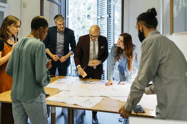 Male and female entrepreneurs discussing over blueprint on table in office - JRFF04859