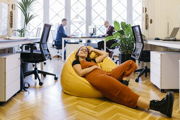 Smiling businesswoman resting on bean bag in office - JRFF04868