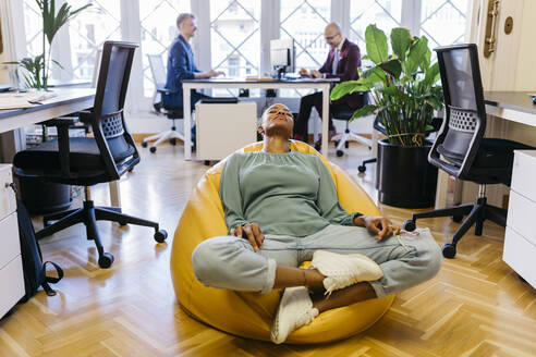 Müde Geschäftsfrau mit geschlossenen Augen ruht auf Sitzsack im Büro - JRFF04869