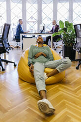 Smiling businesswoman with eyes closed resting on bean bag in office - JRFF04870