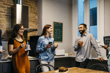 Smiling male and female entrepreneurs discussing while having coffee in kitchen at workplace - JRFF04885