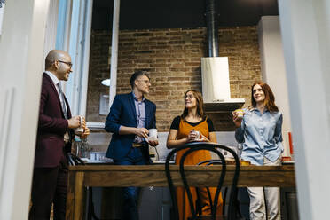 Low angle view of male and female entrepreneurs discussing while having coffee in office kitchen - JRFF04886