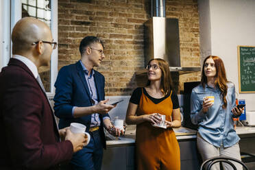 Male and female colleagues discussing while having coffee in office kitchen - JRFF04887