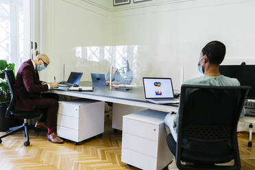 Geschäftsleute mit Schutzmaske bei der Arbeit am Schreibtisch im Büro - JRFF04890