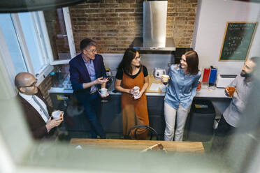 High angle view of smiling business professionals discussing while having coffee in office kitchen seen through glass window - JRFF04909