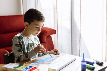 Junge malt in den Sommerferien zu Hause über den Tisch - XLGF00733