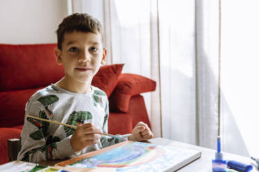 Junge mit Pinsel am Tisch zu Hause in den Sommerferien - XLGF00734