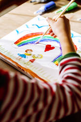 Hand of girl painting rainbow over table at home - XLGF00736