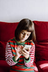 Mädchen, das ein Smartphone benutzt, während es auf dem Sofa im Wohnzimmer sitzt - XLGF00746