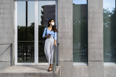 Junge Frau mit Gesichtsschutz am Eingang eines Gebäudes während COVID-19 - AFVF07463