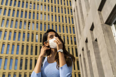 Young businesswoman wearing face mask against office building during COVID-19 outbreak - AFVF07465