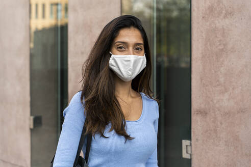 Businesswoman in protective face mask by building during COVID-19 - AFVF07466