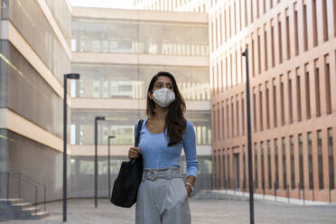 Geschäftsfrau mit Gesichtsmaske schaut weg, während sie vor einem Bürogebäude steht - AFVF07470