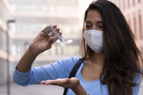Businesswoman in face mask pouring sanitizer on hand during COVID-19 - AFVF07472