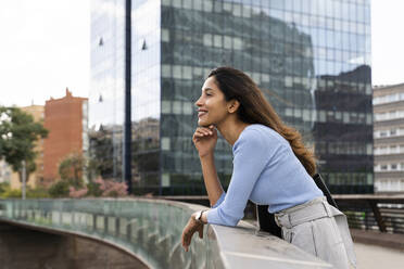 Nachdenkliche junge Geschäftsfrau lehnt am Geländer einer Fußgängerbrücke - AFVF07503
