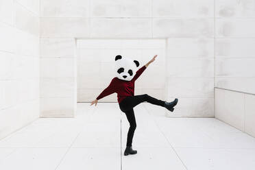 Frau mit hochgelegtem Bein, die eine Panda-Maske trägt und vor einer Tür steht - XLGF00762