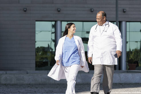 Doctors wearing lab coat walking against hospital - GGGF00037