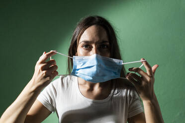 Woman wearing protective face mask against green wall during COVID-19 crisis - GIOF09528