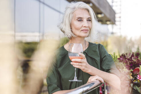 Reife Frau trinkt Saft, während sie am Geländer eines Restaurants steht - VYF00214