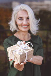 Lächelnde reife Frau, die ein Geschenk hält, während sie im Restaurant steht - VYF00217