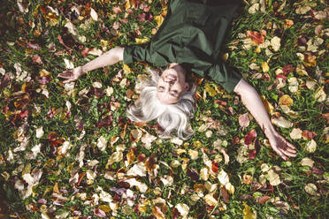 Reife Frau lächelnd auf Gras im Park liegend - VYF00233