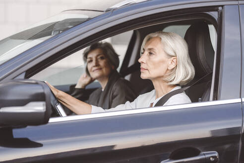 Colleague sitting with businesswoman while driving car in city - VYF00279