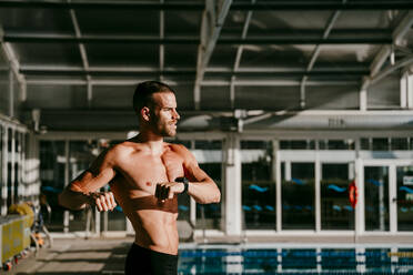 Hemdloser männlicher Schwimmer bei einer Aufwärmübung am Beckenrand - EBBF01282