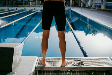 Junger männlicher Schwimmer am Beckenrand stehend - EBBF01283