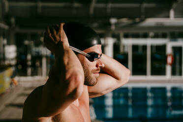 Hübscher männlicher Schwimmer, der sich an einem sonnigen Tag auf das Schwimmen vorbereitet - EBBF01288