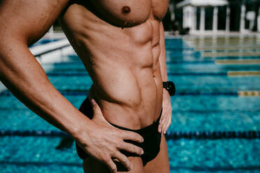 Männlicher Schwimmer mit Bauchmuskeln am Beckenrand stehend an einem sonnigen Tag - EBBF01309