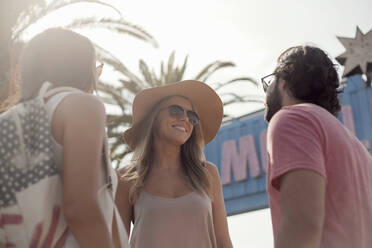 Lächelnde männliche und weibliche Freunde mit Sonnenbrillen unterhalten sich an einem sonnigen Tag - AJOF00500