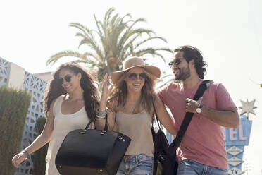 Lächelnde männliche und weibliche Freunde mit Sonnenbrillen gehen gegen den Himmel an einem sonnigen Tag - AJOF00501