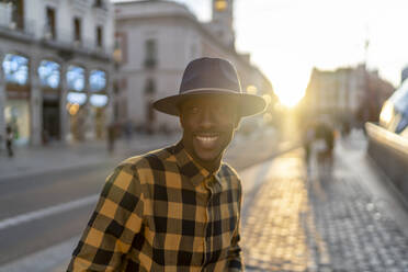 Lächelnder afrikanischer Mann bei Sonnenuntergang auf dem Gehweg stehend - PGF00166